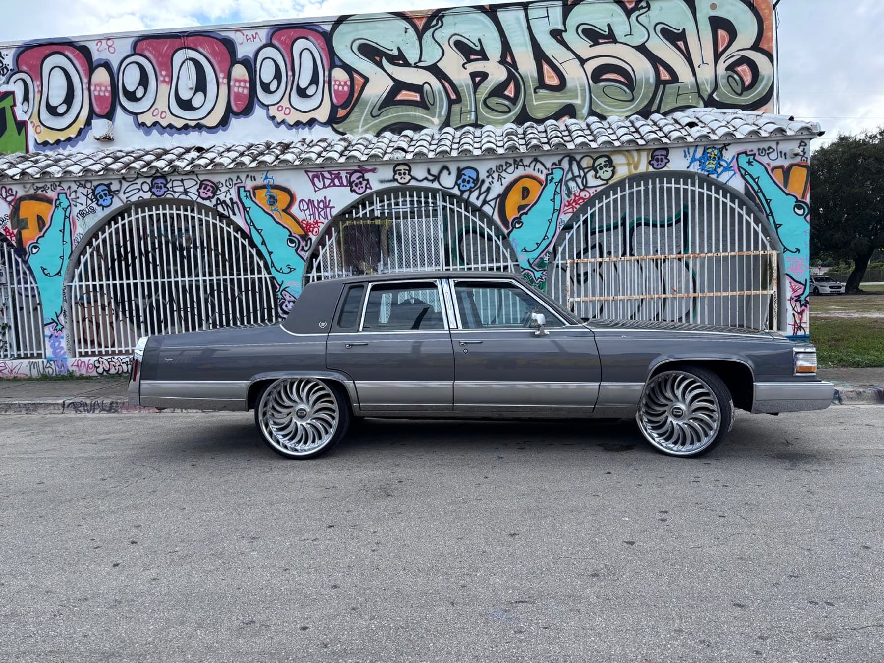 Gray classic Chevy-style sedan in front of a Miami mural with polished wheels